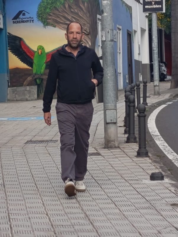 James Roberts walking along a street in Tenerife, past a mural of a green parrot